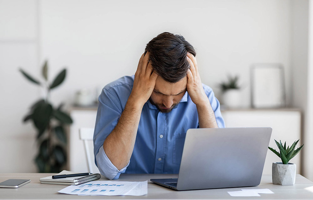 Business man looking frustrated in front of a laptop.