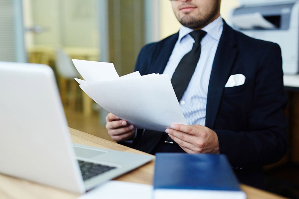 Business person reading paper documents in front of laptop
