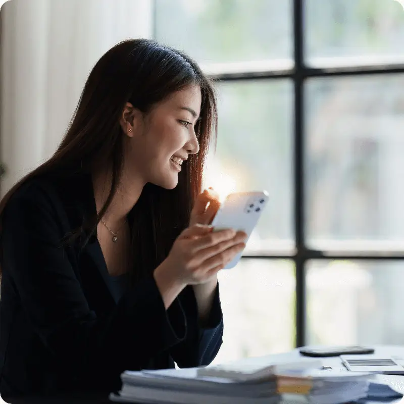 Asian Female smiles while looking out window with work papers on table.